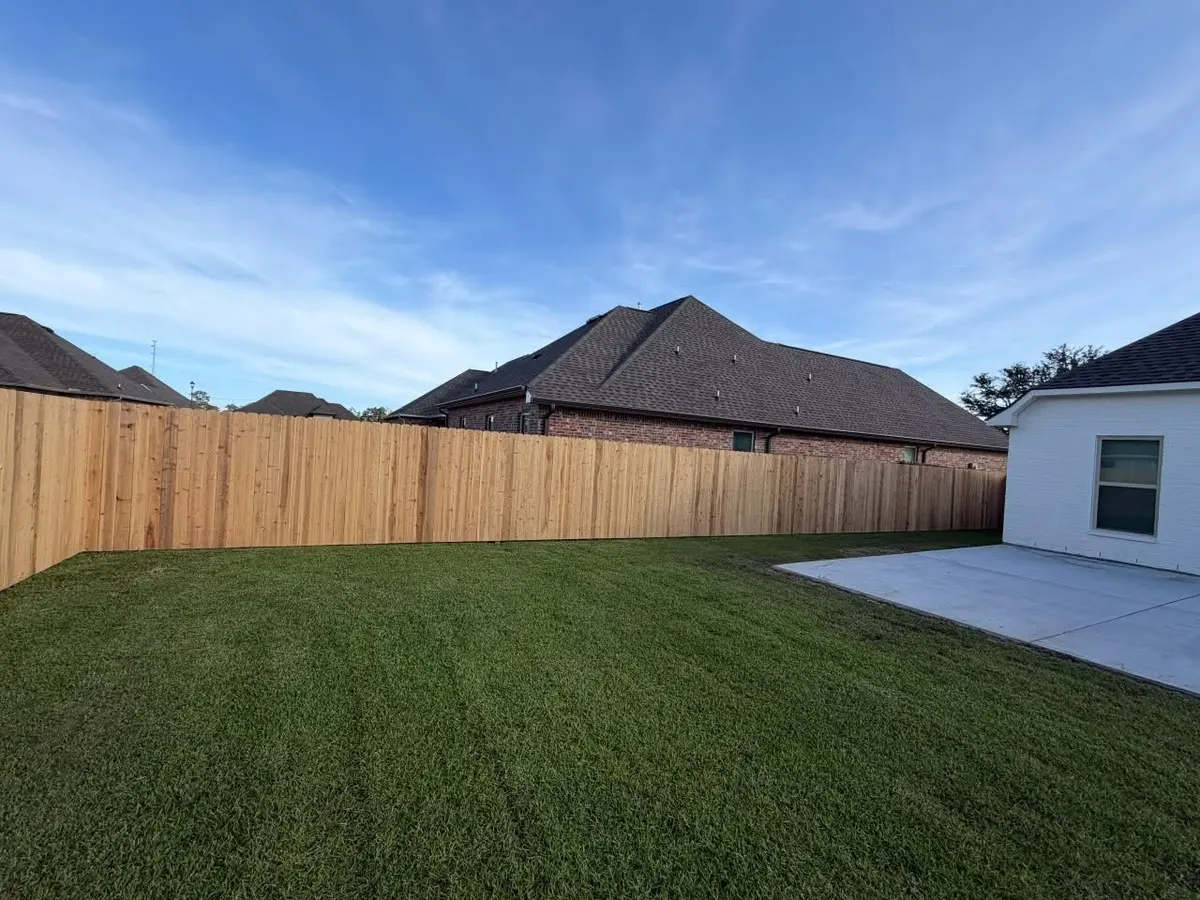 Cedar privacy fence enclosing a backyard behind a white brick home
