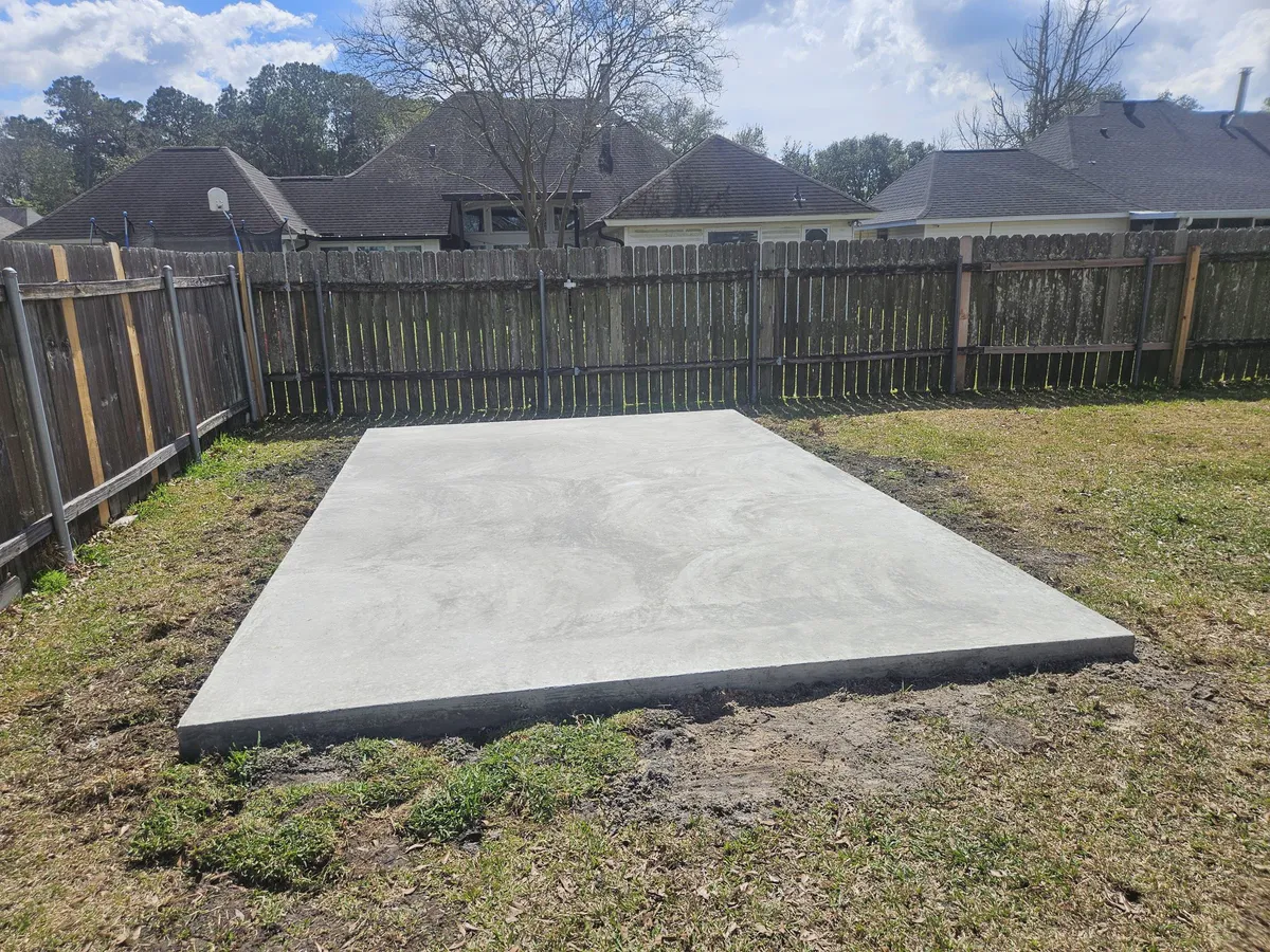 Concrete slab pad in backyard next to wooden fence