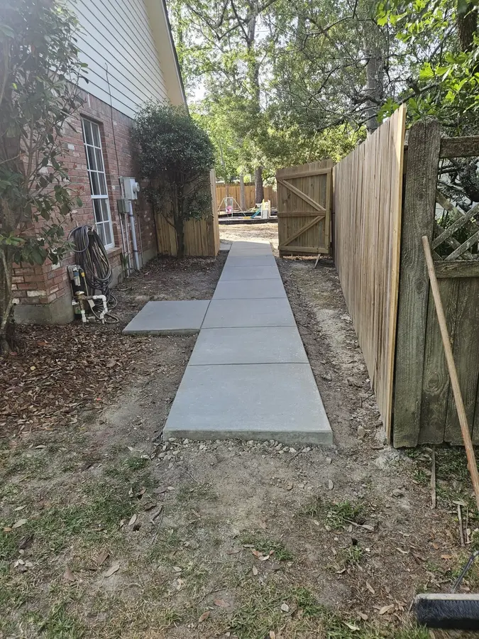 New concrete walkway running along a brick home to a backyard gate